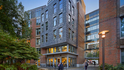 People sitting in a grassy courtyard outside a modern six-story brick residential building