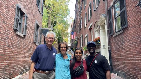 Four people stand shoulder to shoulder between two historic red-brick buildings