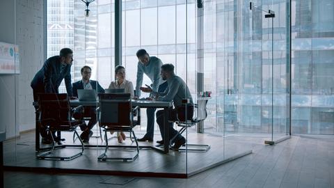 A group of people having a discussion around a table in a glass conference room