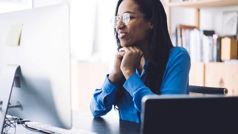 A smiling woman wearing glasses watches a webinar on her computer screen