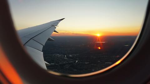 Looking out an airplane window over the wing at the sun setting over the horizon