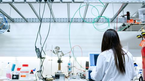 A chemical engineer in a white lab coat works at a monitor in a lab
