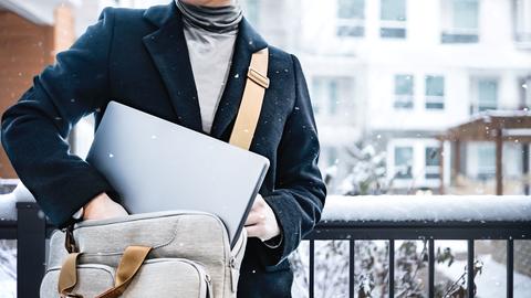 A person in a winter coat puts a laptop into a travel bag while snow lightly falls