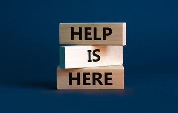 Three wooden blocks stacked on top of each other. Each block is printed with one word so together they say "Help Is Here."