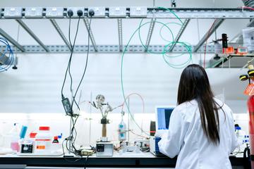 A chemical engineer in a white lab coat works at a monitor in a lab