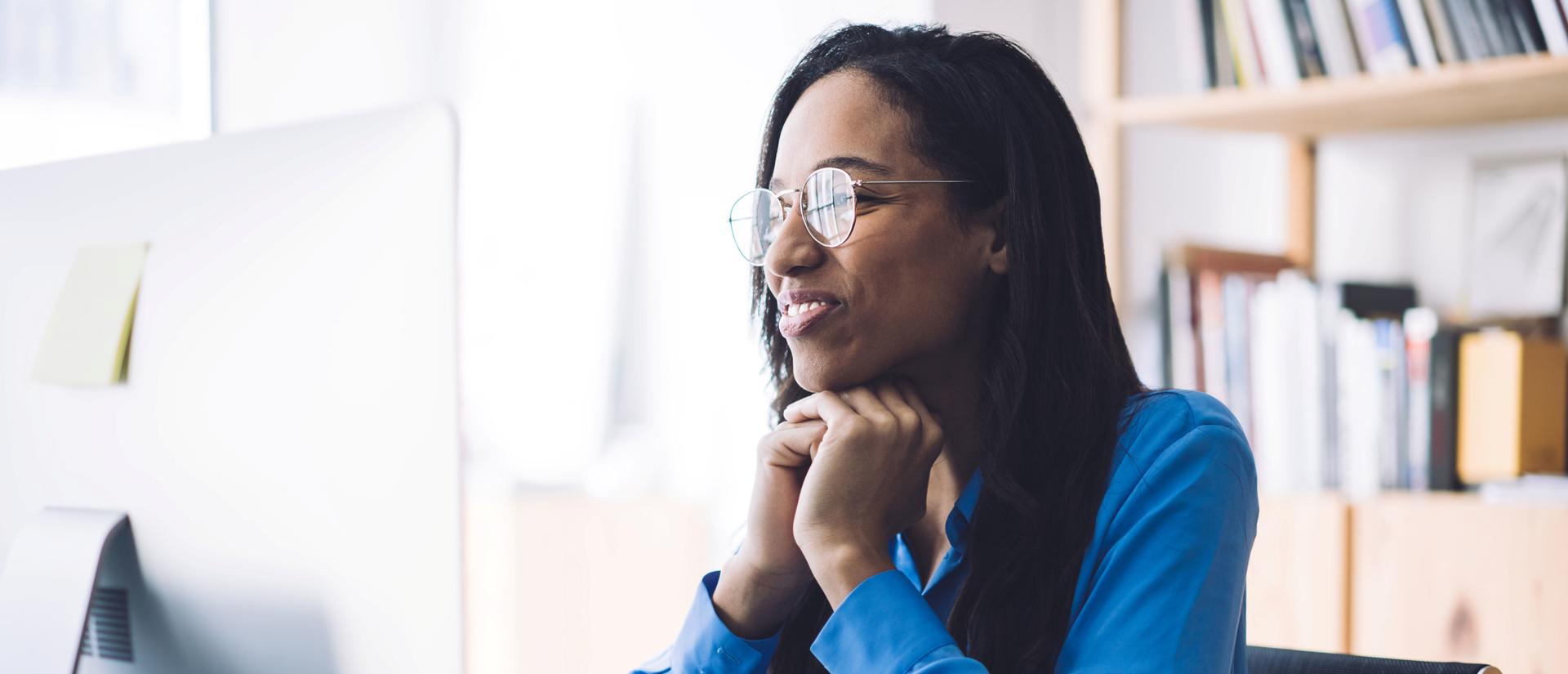 A smiling woman wearing glasses watches a webinar on her computer screen