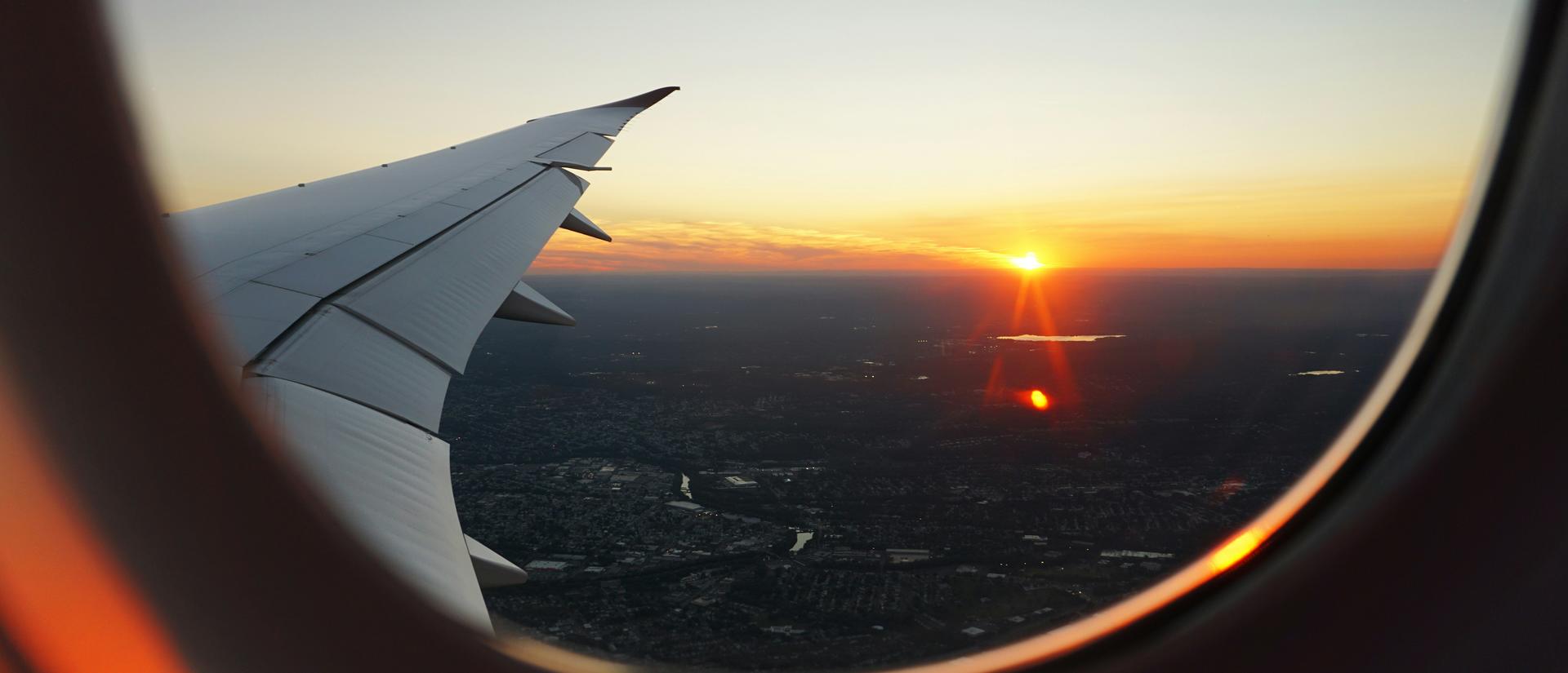 Looking out an airplane window over the wing at the sun setting over the horizon