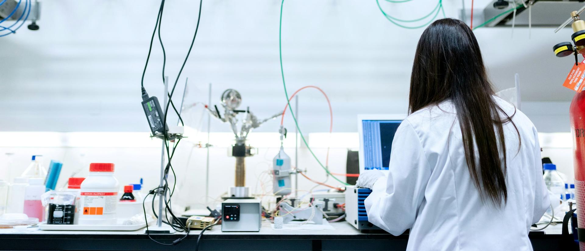 A chemical engineer in a white lab coat works at a monitor in a lab