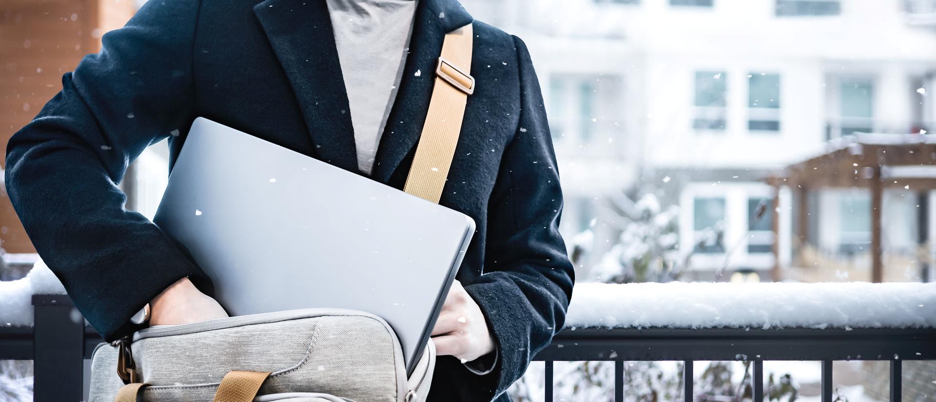 A person in a winter coat puts a laptop into a travel bag while snow lightly falls