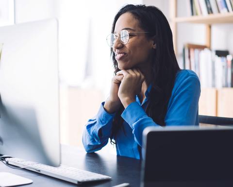 A smiling woman wearing glasses watches a webinar on her computer screen
